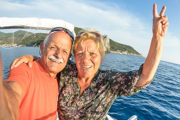 Adventurous senior couple taking selfie at Giglio Island on luxury speedboat - Active elderly travel lifestyle concept on happy tour moment - Retired people around world - Warm afternoon color tones